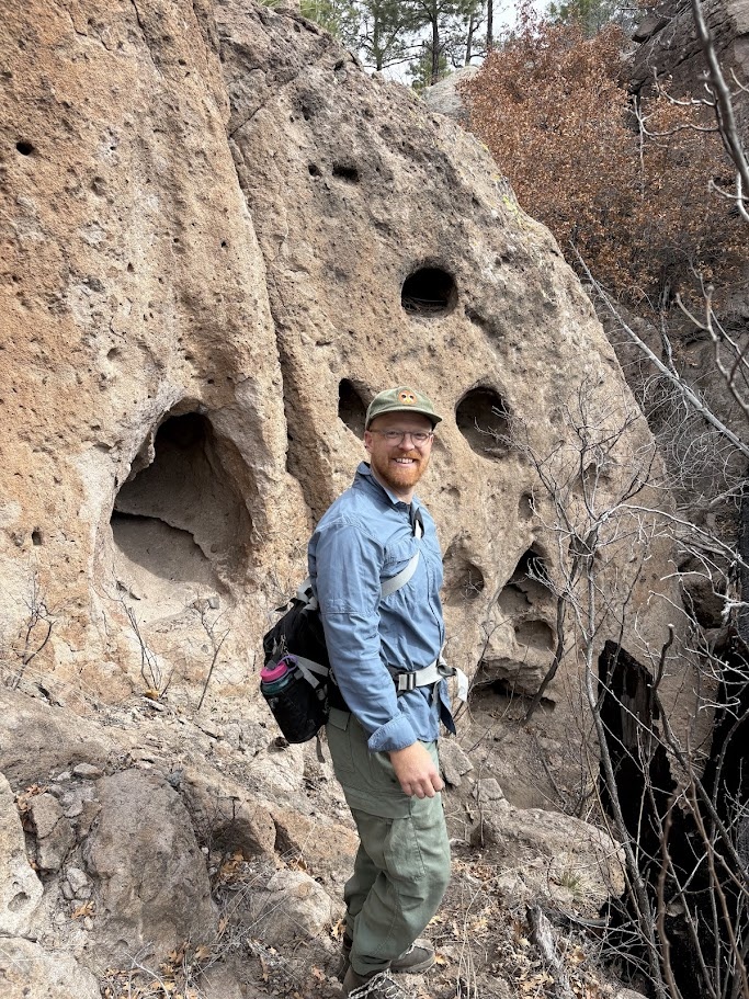 Gavin poses in front of a cliff wall with characteristic Bandelier Tuff “swiss cheese” potholes, which sometimes are perfect homes for Mexican spotted owls!