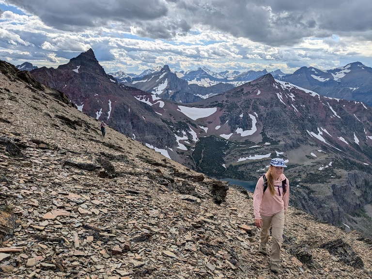 Dani Owens traverses a slope in front of a sea of peaks and clouds in Glacier National Park, MT.
